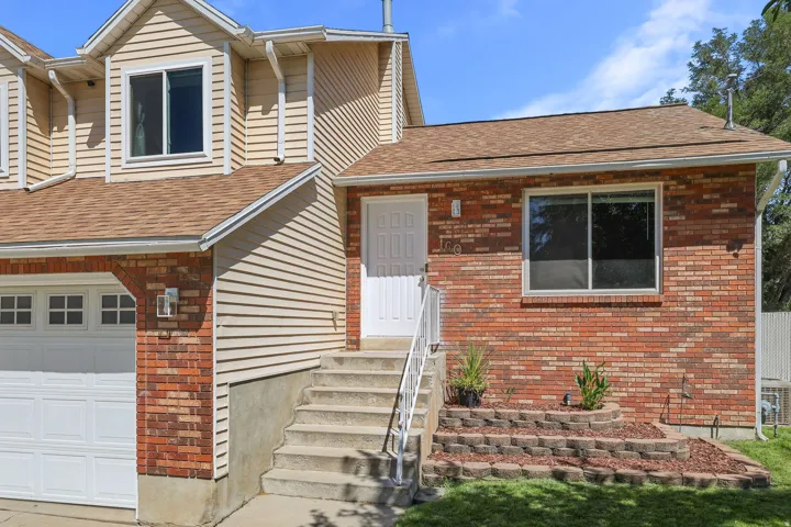 Exterior featuring brick and siding finishes, a shingle roof, attached garage with white door, and tiered landscaping