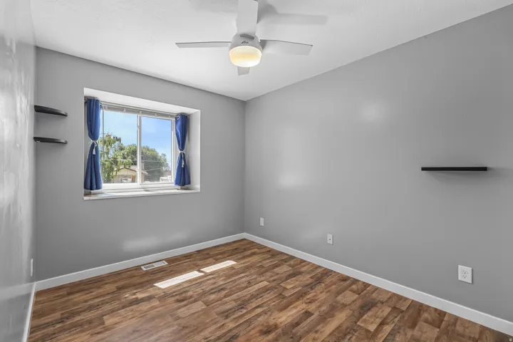 Wood-finish flooring, ceiling fan with integrated lighting, window with a white frame, and gray painted walls