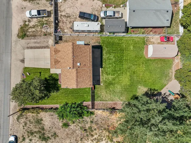Extensive green lawn, concrete driveway, mature trees, brown shingle roofing, and a detached shed