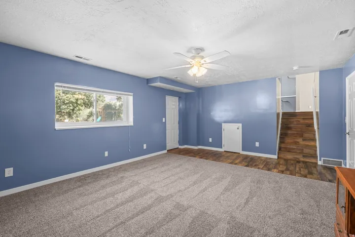 Spacious room with plush carpeting, wood-finish flooring, and a ceiling fan