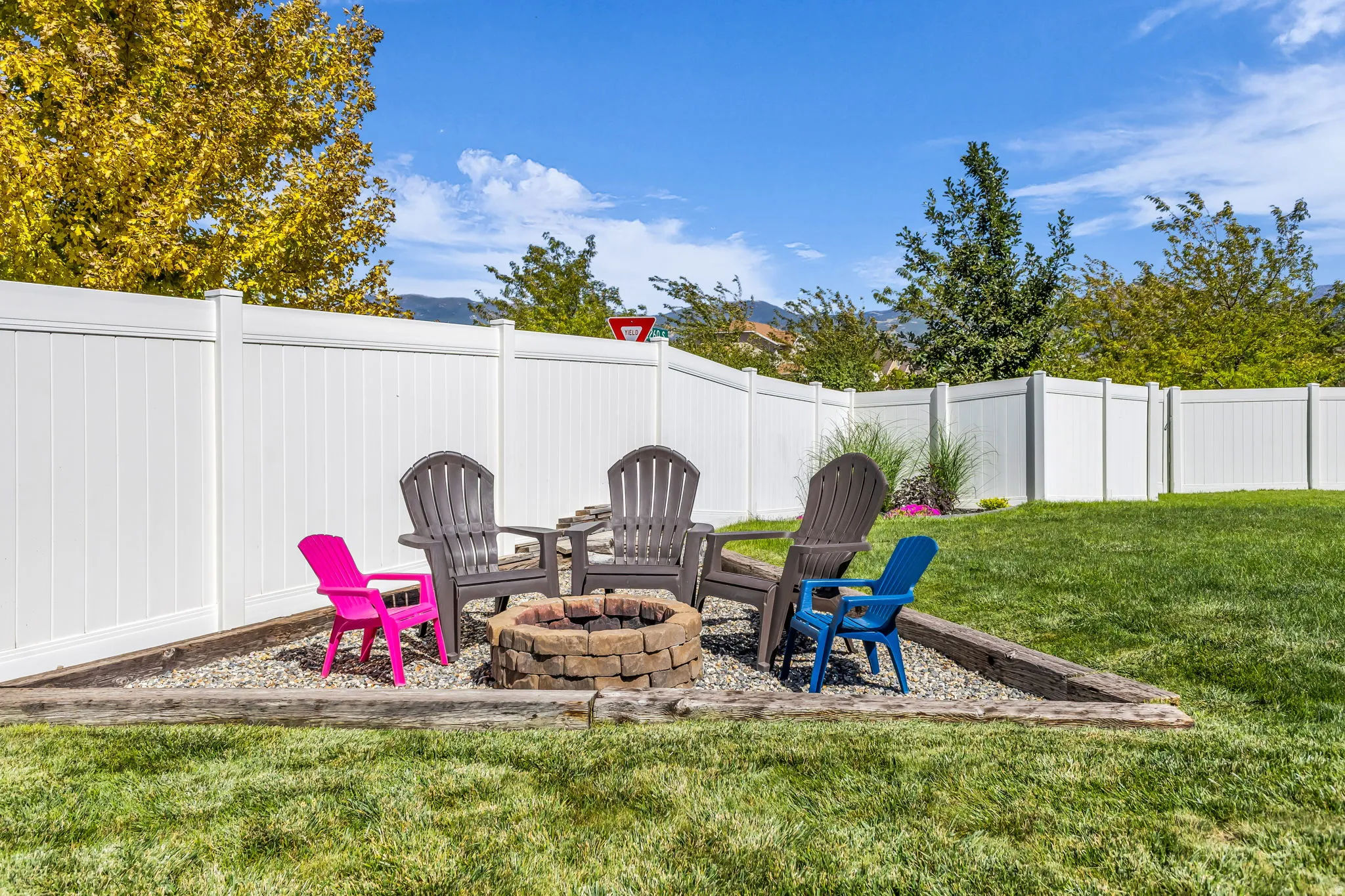 Private backyard with a white panel fence, stone fire pit, and landscaped gravel area