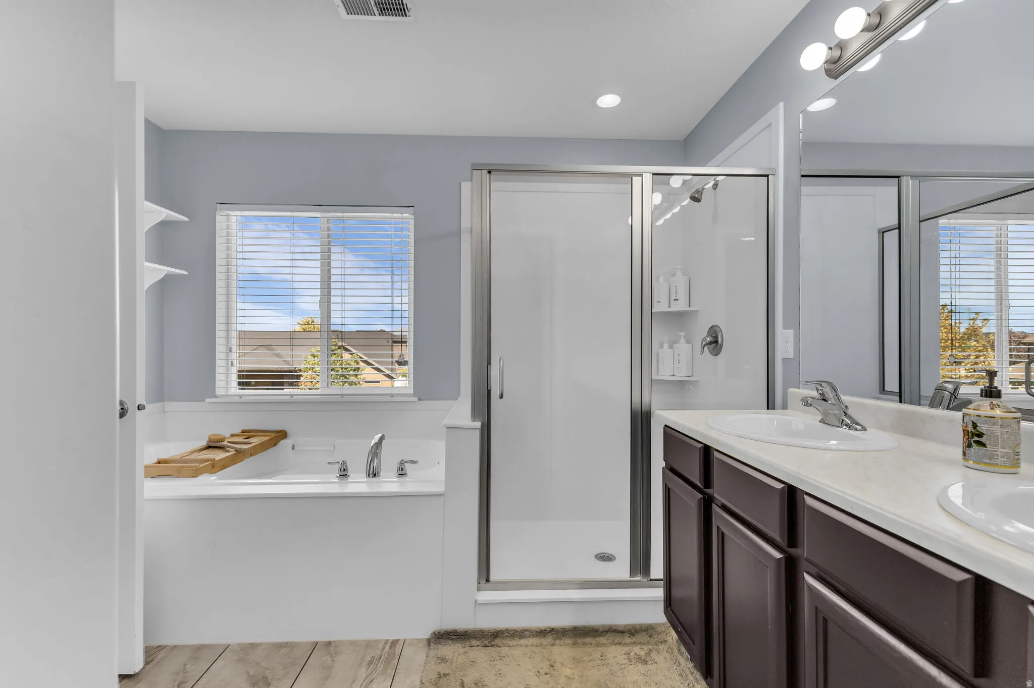 Recessed lighting, wood-finish flooring, built-in soaking tub, glass-enclosed shower, and dual vanity with integrated sinks