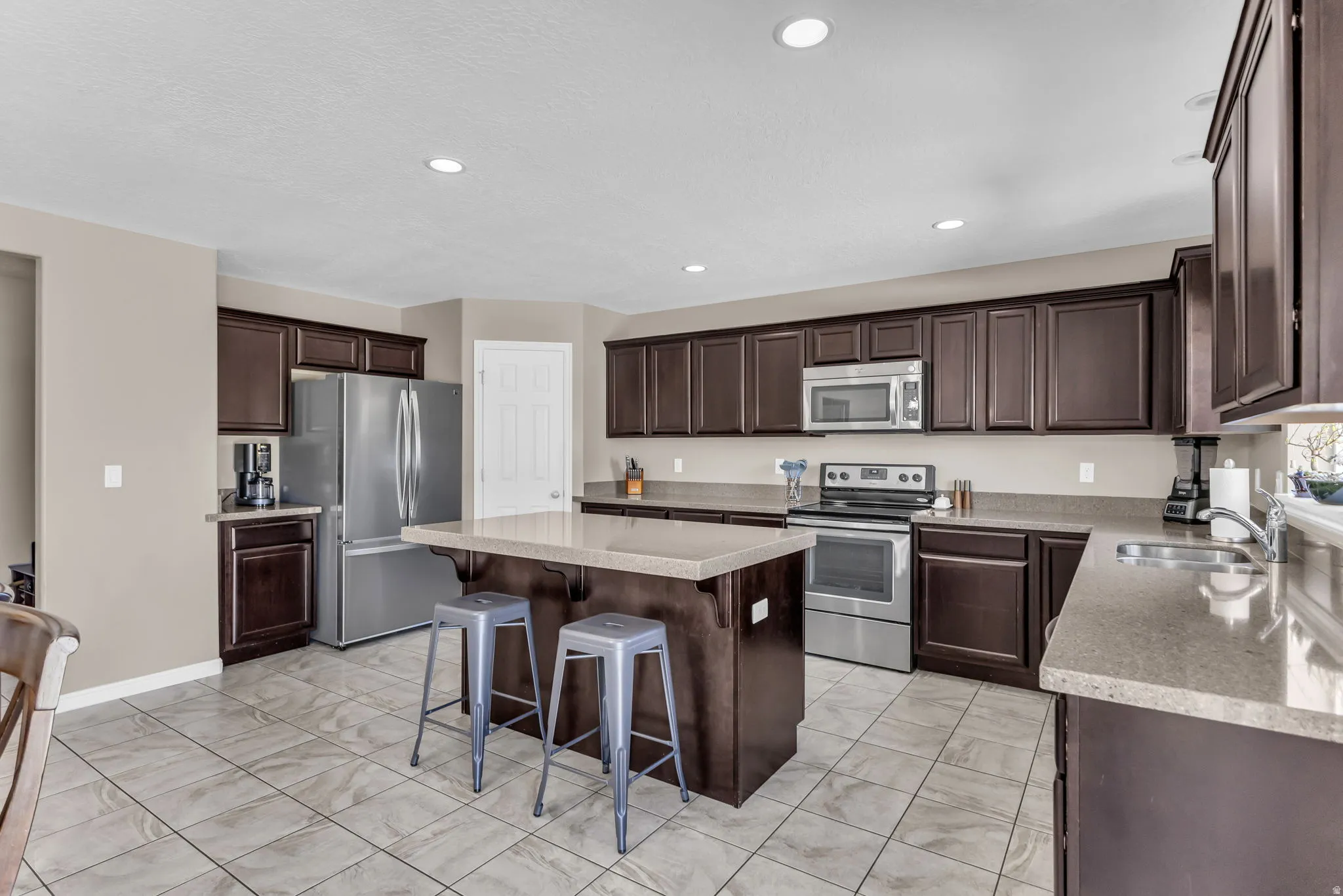 Kitchen featuring dark wood cabinetry, stainless steel appliances, a center island with countertop seating, and tile flooring