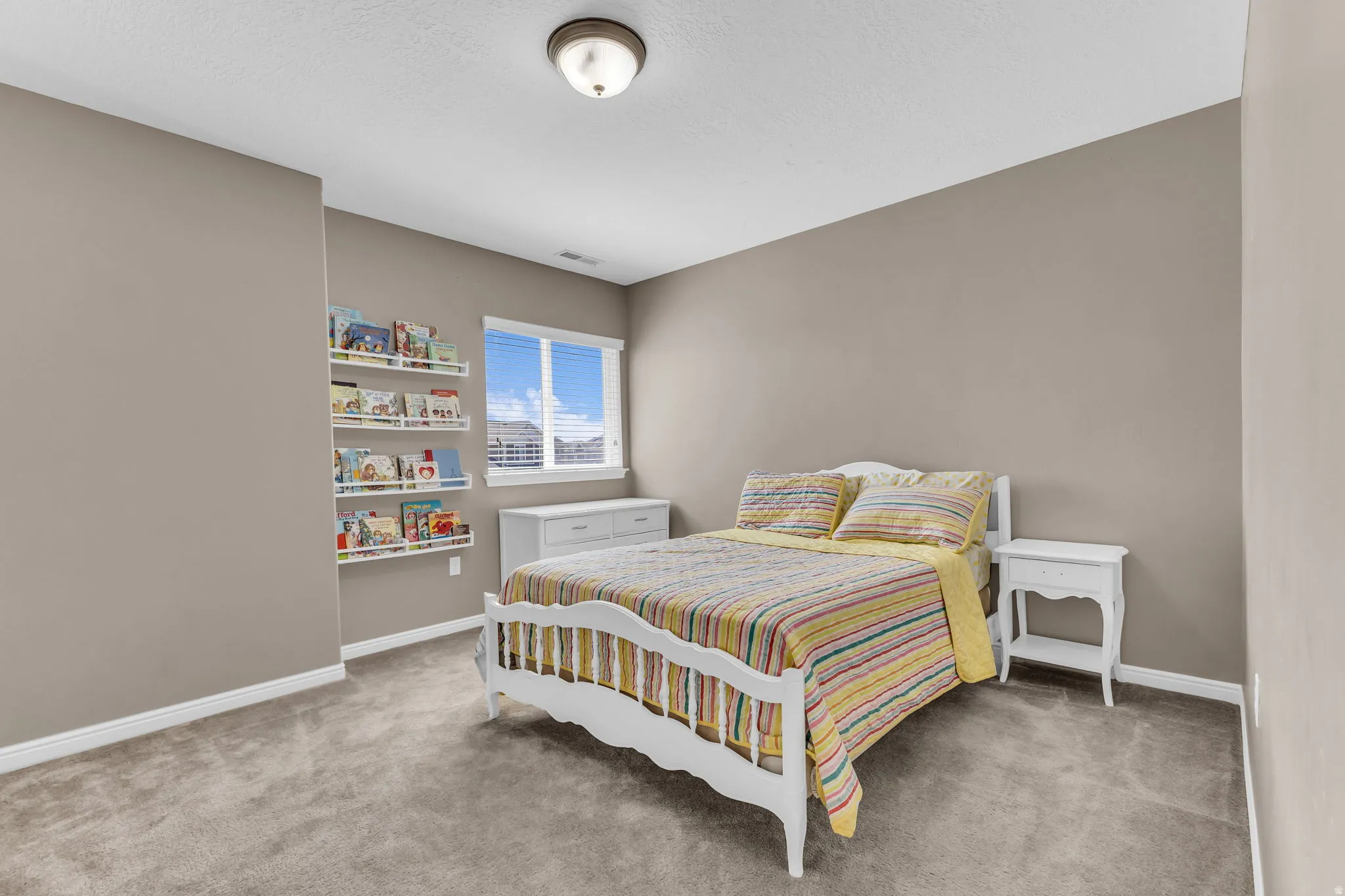 Plush carpet flooring, recessed window with blinds, wall-mounted light fixture, and built-in shelving