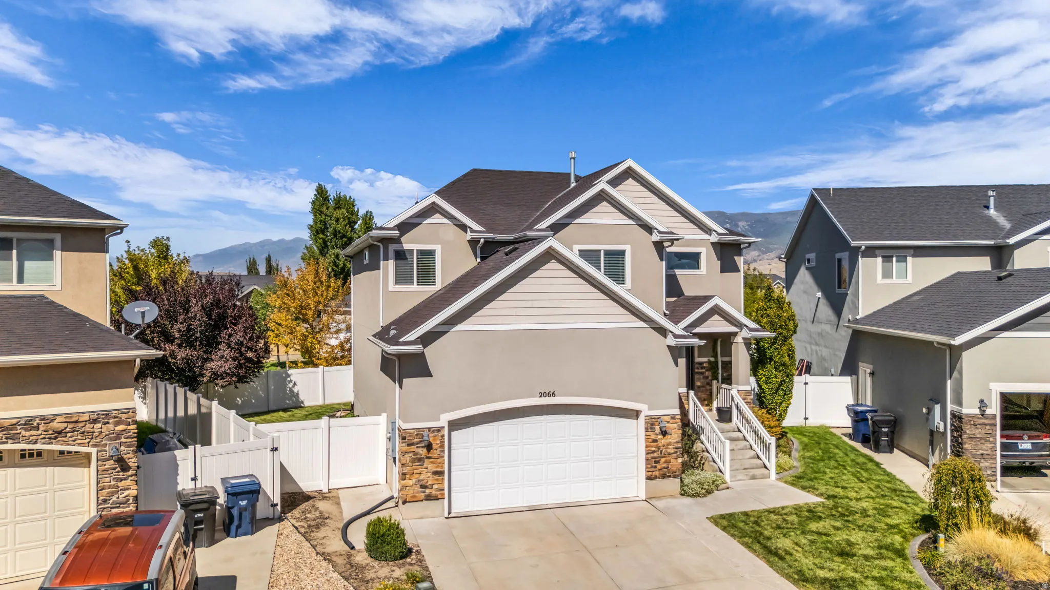 Stucco and stone exterior with a two-car garage, concrete driveway, and a white fence