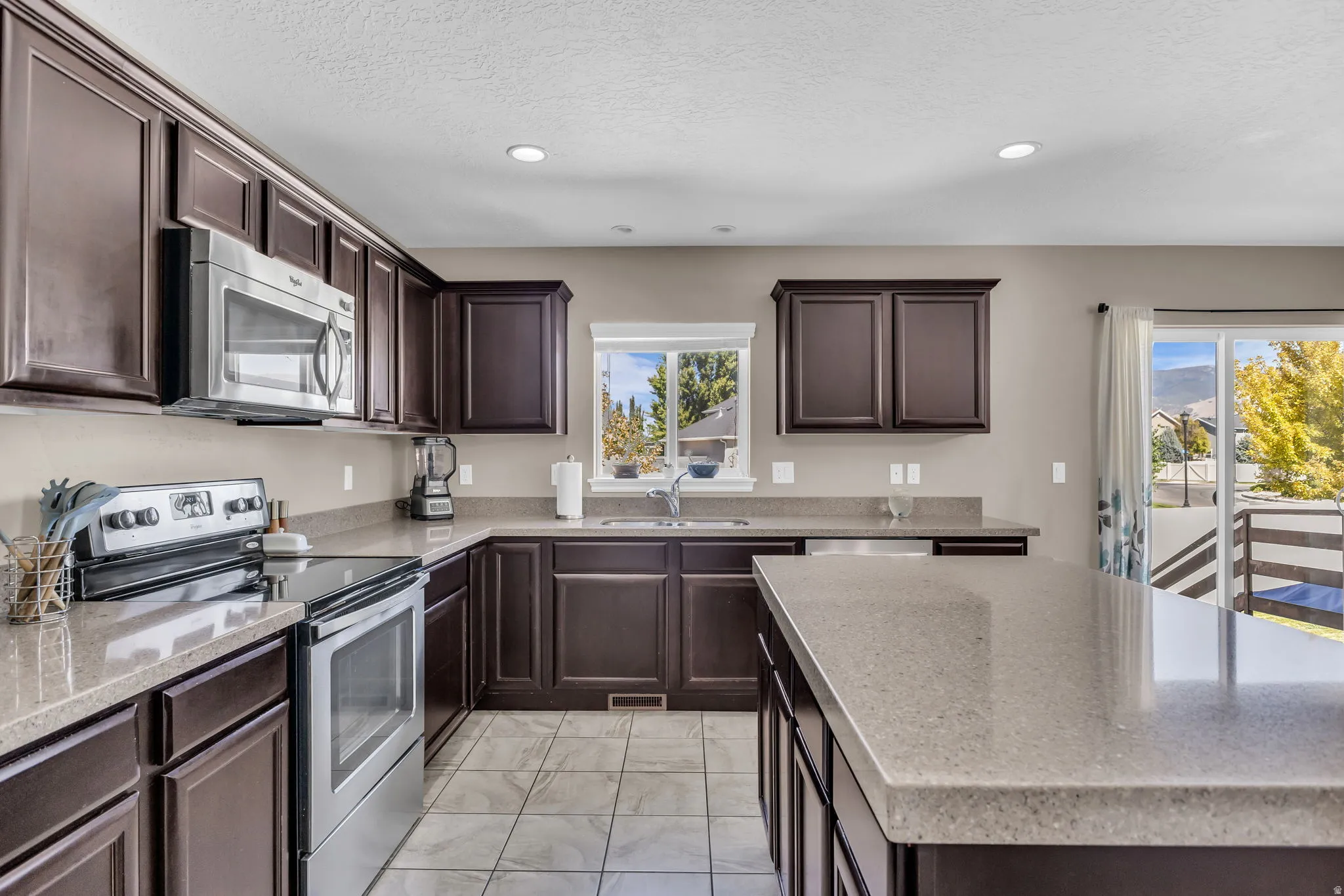 Kitchen with dark wood cabinetry, light-toned countertops, stainless steel appliances, and tiled flooring