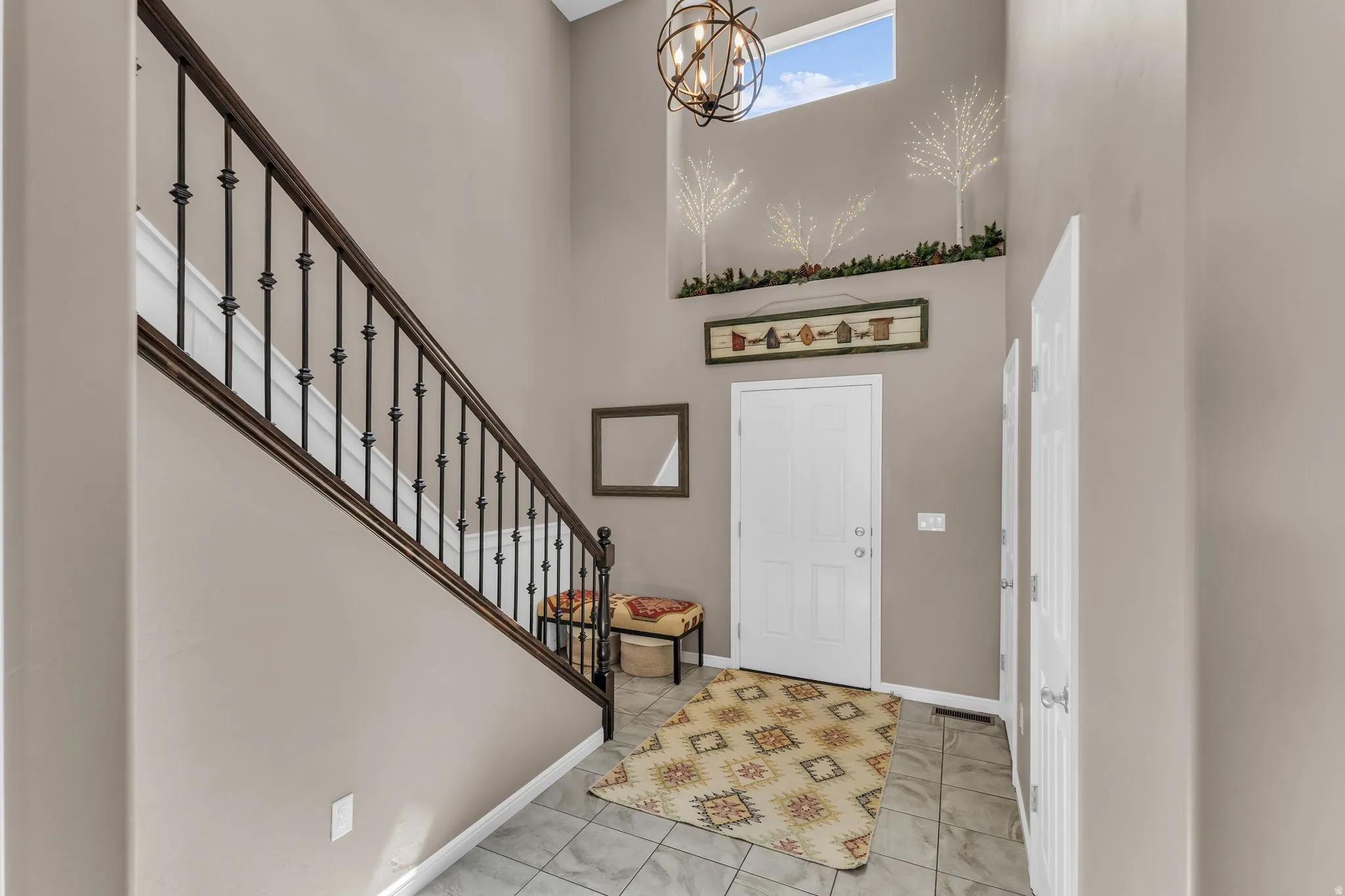 Two-story foyer with high ceilings, wrought iron staircase railing, overhead chandelier, and a transom window