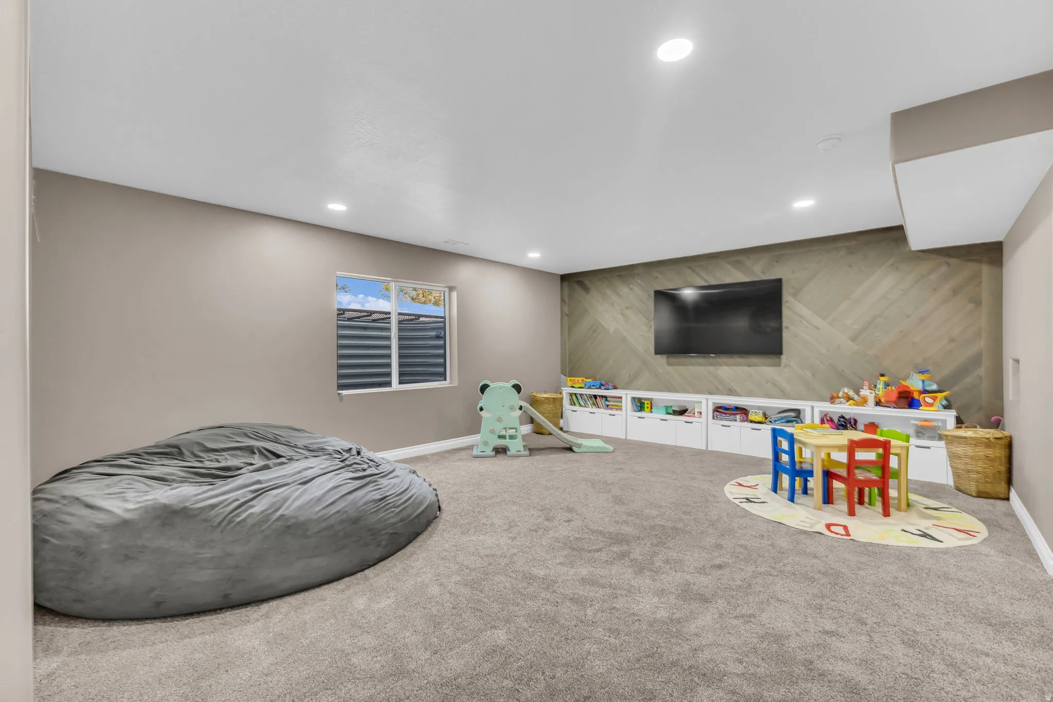 Spacious room featuring neutral carpeting, recessed lighting, a window, built-in white cabinetry, and a decorative wood-paneled accent wall