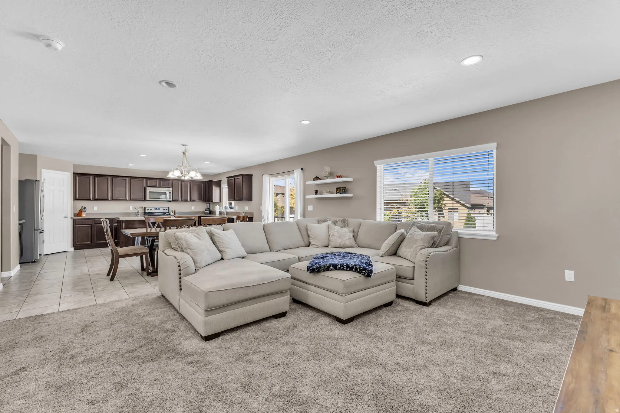 Spacious open-concept living area with plush carpeting, recessed lighting, and a large window