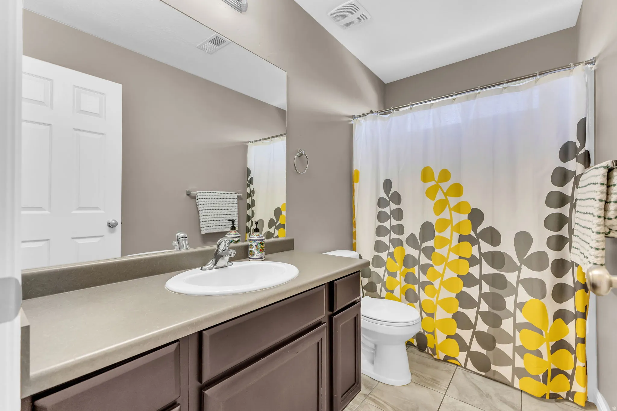 Rectangular mirror, single vanity with integrated sink, dark wood-finish cabinetry, tile flooring, and a built-in toilet