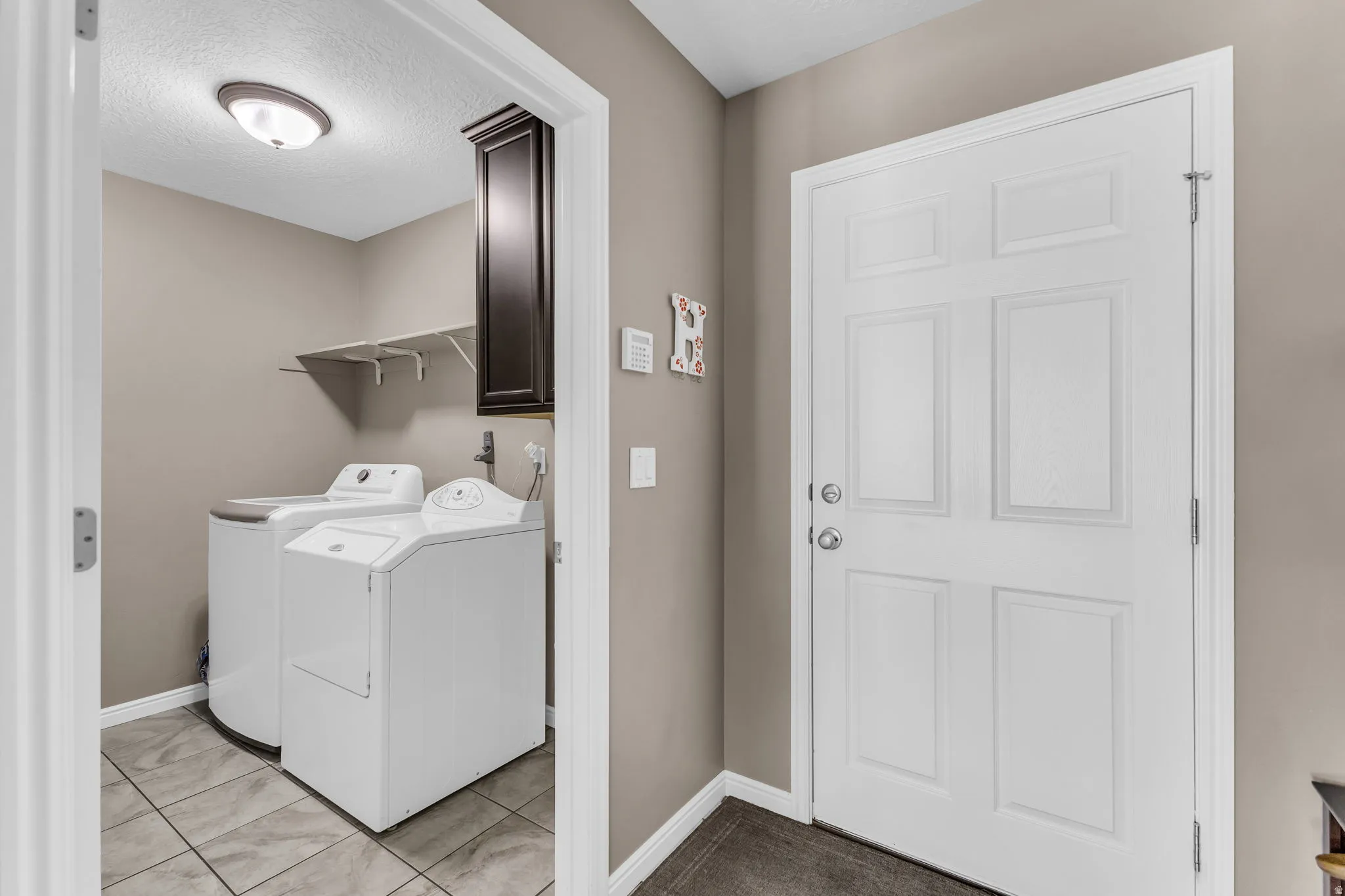 Utility area featuring tile flooring, wall-mounted shelving, and a built-in dark wood-finish cabinet