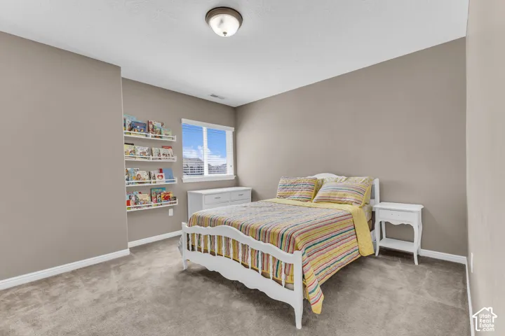 Plush carpet flooring, recessed window with blinds, wall-mounted light fixture, and built-in shelving