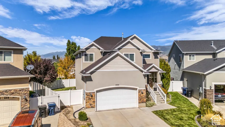 Stucco and stone exterior with a two-car garage, concrete driveway, and a white fence