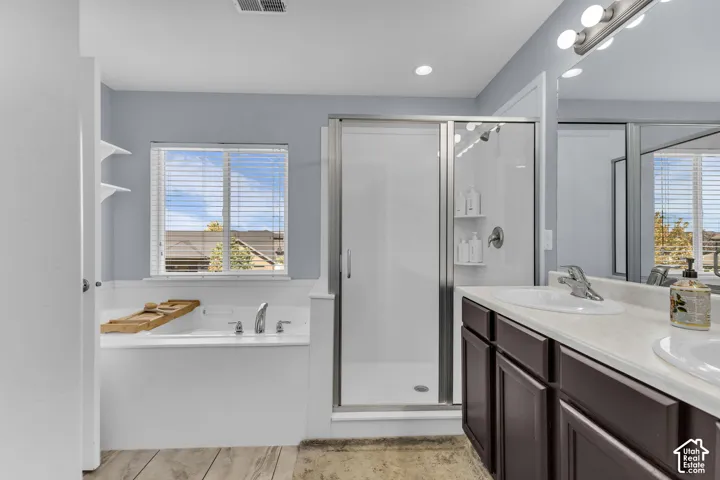 Recessed lighting, wood-finish flooring, built-in soaking tub, glass-enclosed shower, and dual vanity with integrated sinks