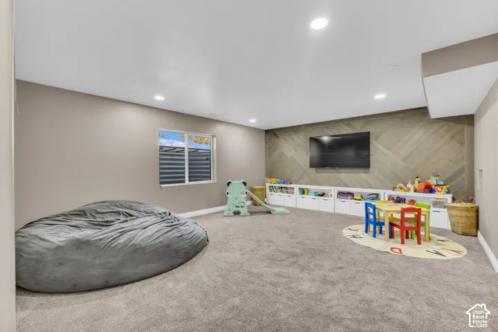 Spacious room featuring neutral carpeting, recessed lighting, a window, built-in white cabinetry, and a decorative wood-paneled accent wall