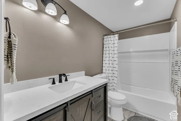 White countertop with integrated sink, black matte faucet, wood-finish vanity with barn door hardware, white bathtub with shower, and tile flooring