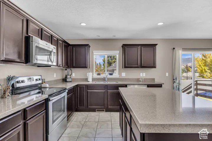 Kitchen with dark wood cabinetry, light-toned countertops, stainless steel appliances, and tiled flooring