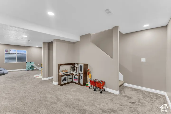Carpeted room with recessed lighting, neutral wall tones, a visible window, and a staircase