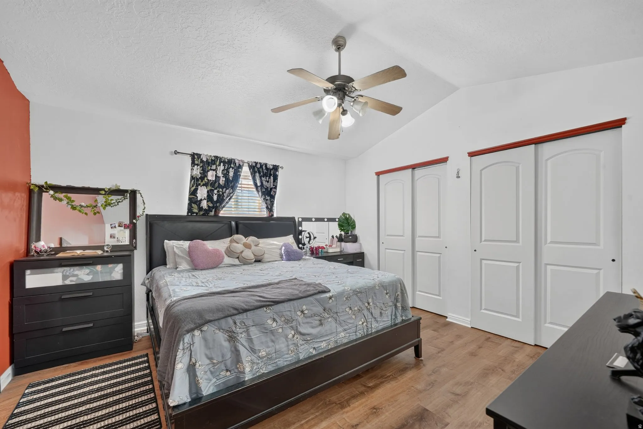 Vaulted ceiling, wood-finish flooring, ceiling fan with integrated lighting, window with blinds, and white sliding closet doors