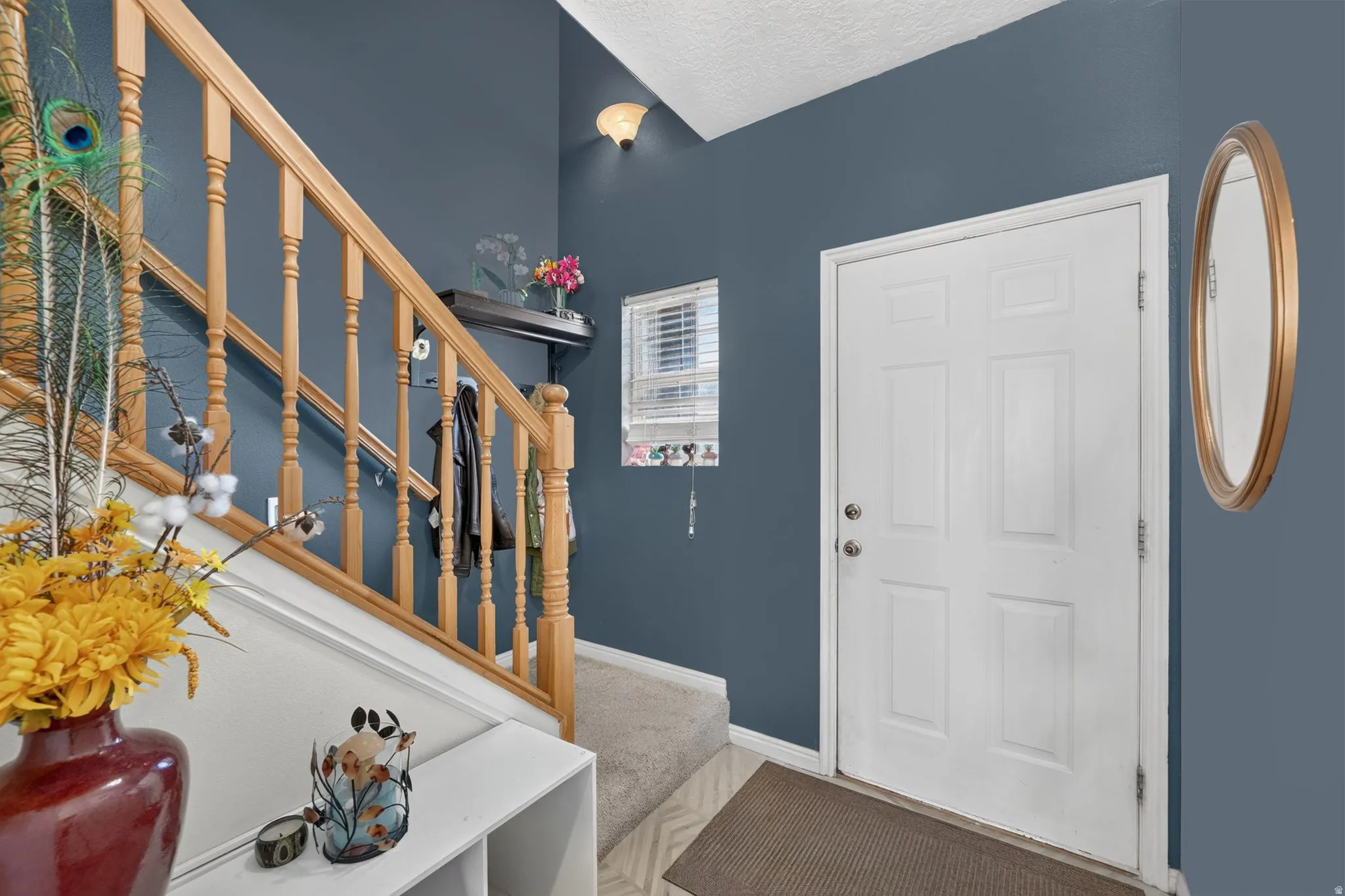 Entryway featuring a paneled door, wood staircase, wall-mounted light fixture, and window with blinds