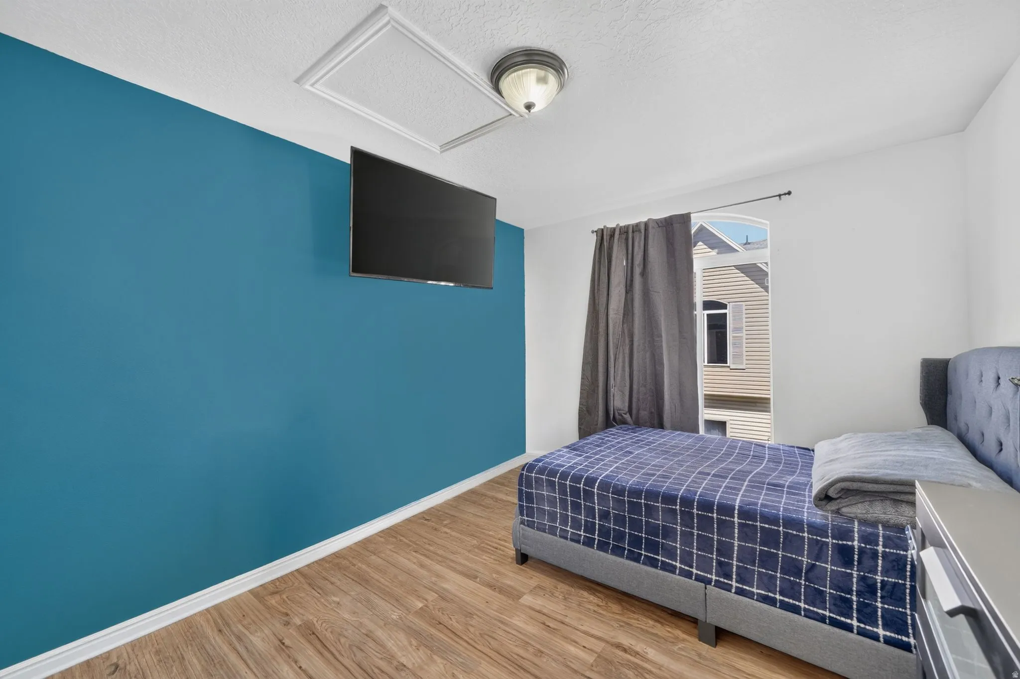 Wood-finish flooring, accent wall, ceiling-mounted light fixture, and window with exterior siding visible