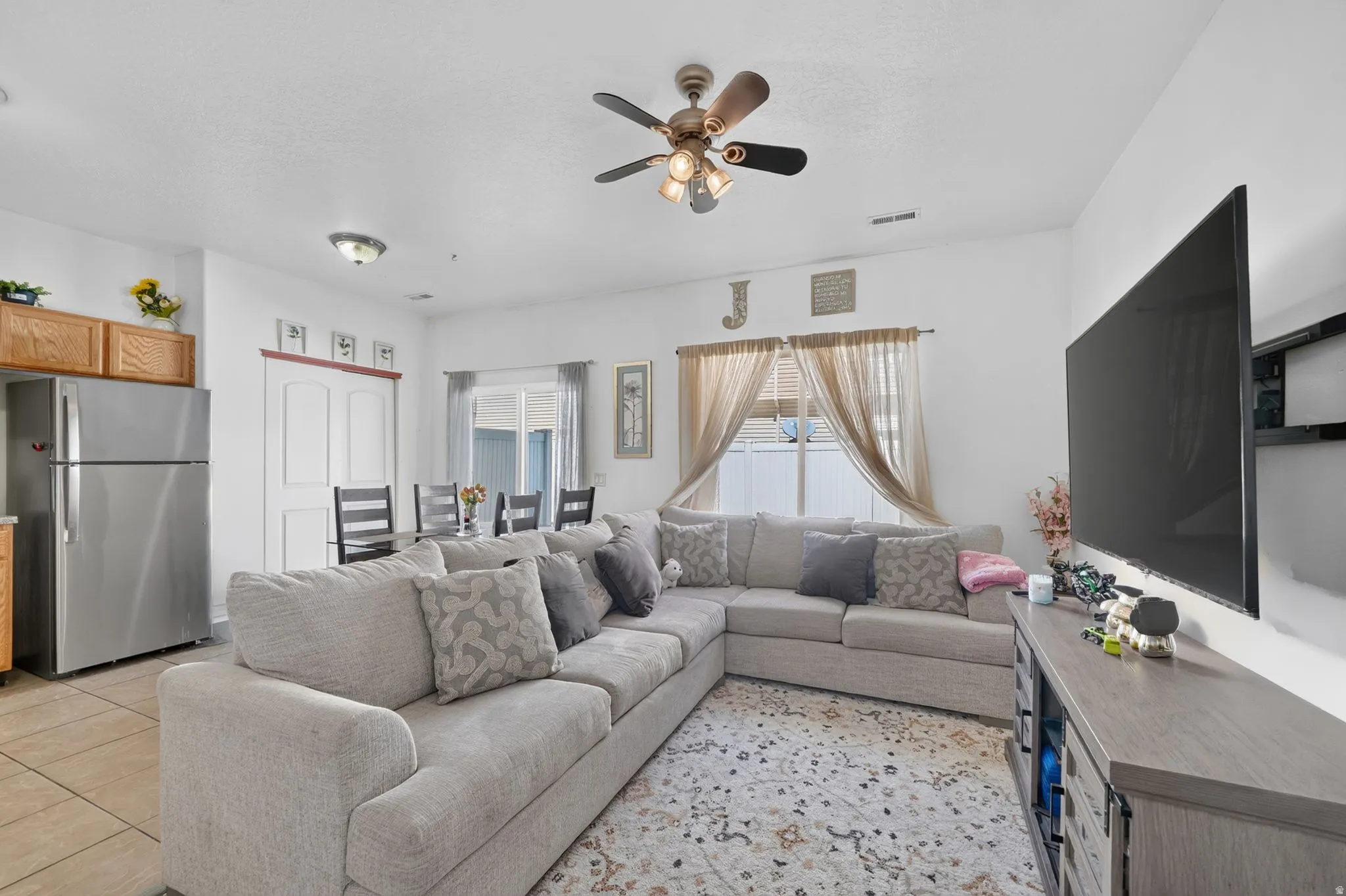 Open-concept living area with tile flooring in the kitchen, wood-finish cabinetry, and stainless steel refrigerator