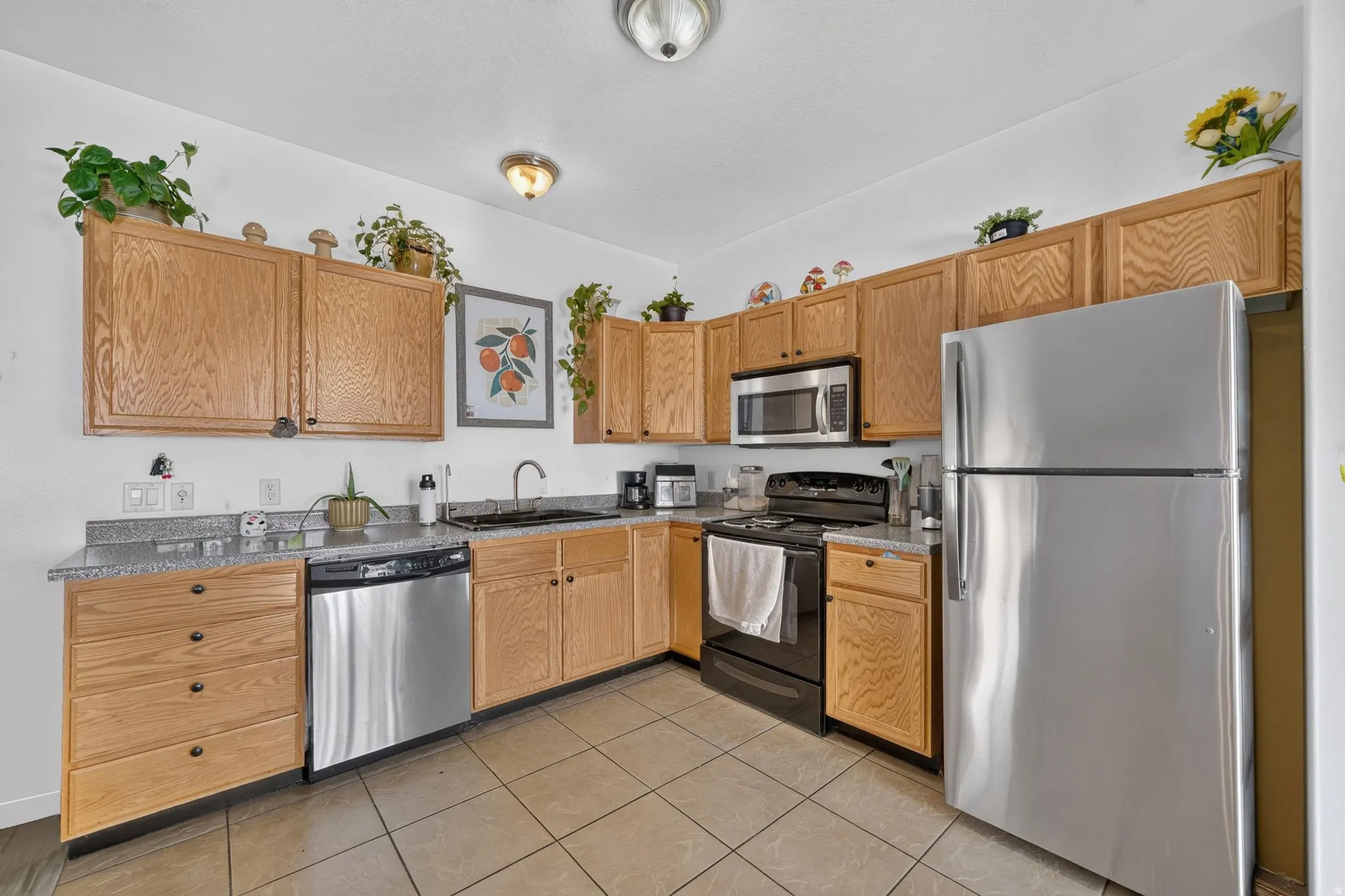 Kitchen featuring wood cabinetry, stainless steel appliances, granite-finish countertops, and tiled flooring