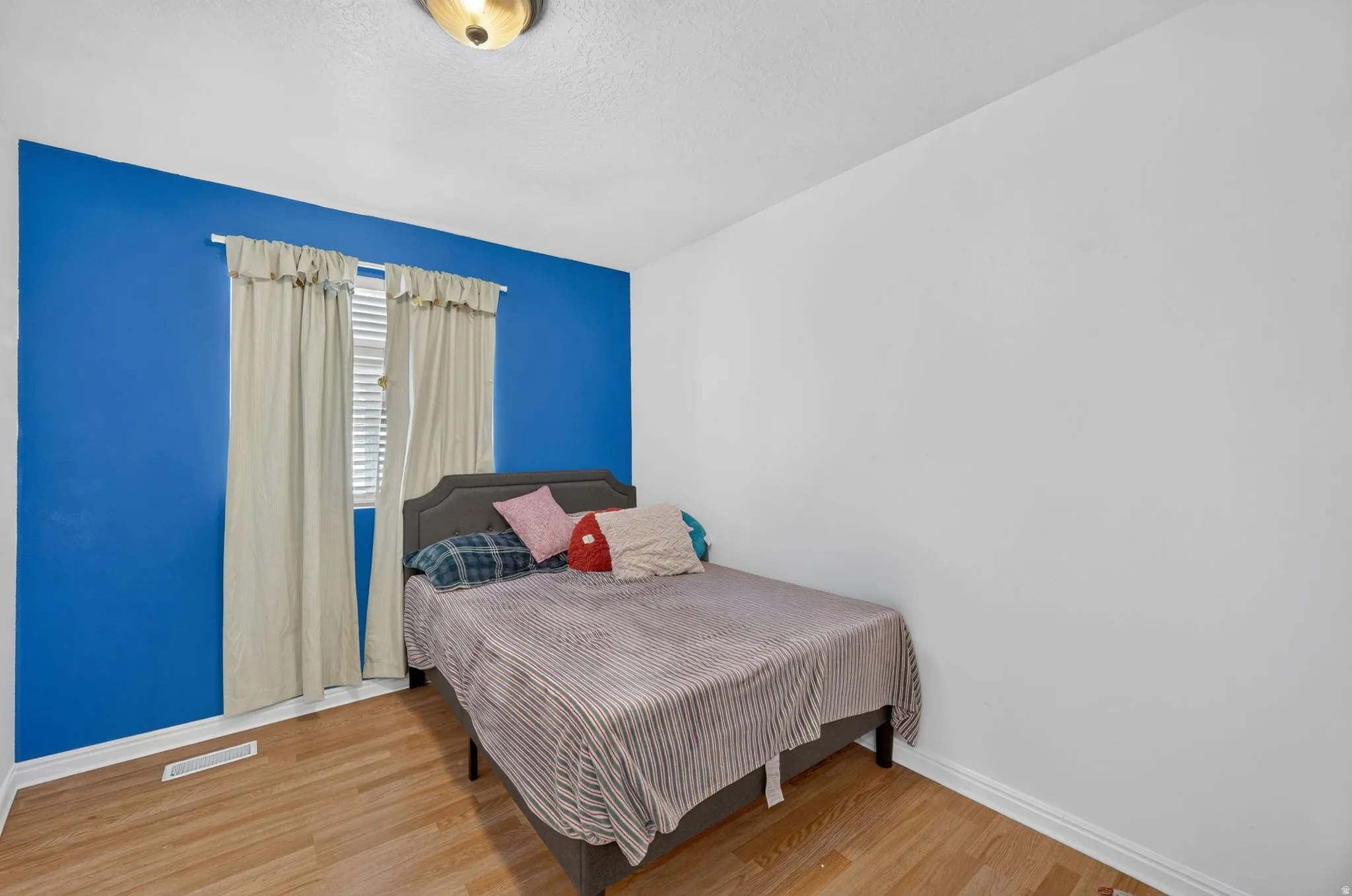 Wood-finish flooring, white walls, recessed window with blinds, and ceiling-mounted light fixture