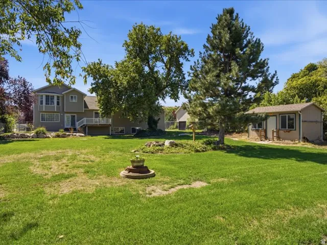 Expansive green lawn, mature trees, multi-level dwelling with bay window, rear deck, and a detached shed structure