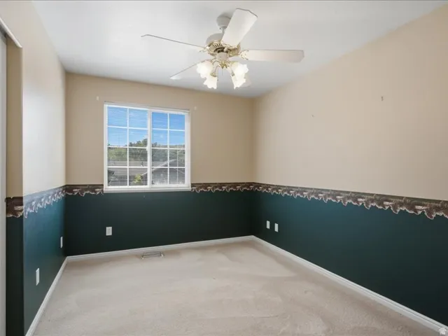 Carpeted room with a ceiling fan, a window, and wall trim