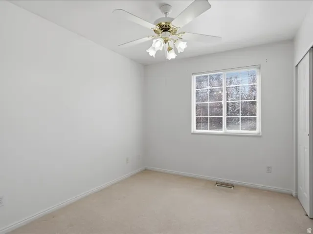 Ceiling fan with light fixture, window with grid panes, wall-to-wall carpeting, and bi-fold closet doors