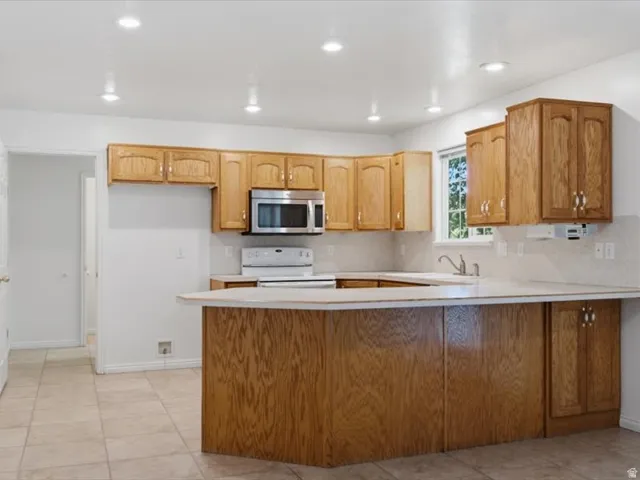 Kitchen featuring wood cabinetry, light-toned countertops, ceramic tile flooring, stainless steel microwave, and recessed lighting