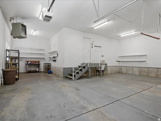 Spacious garage with concrete flooring, built-in shelving, and an elevated storage platform with stairs
