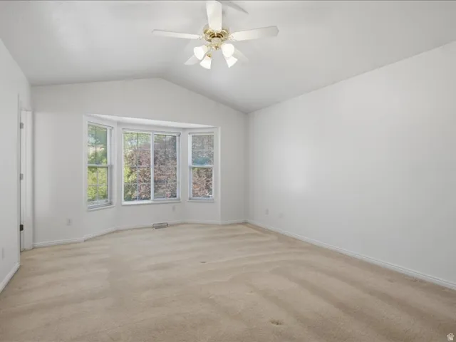 Vaulted ceiling with a ceiling fan, bay window with multiple panes, and neutral carpeting