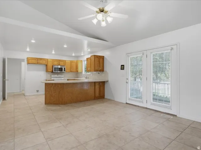 Vaulted ceiling with recessed lighting, wood cabinetry, stainless steel microwave, tile flooring, and double glass doors