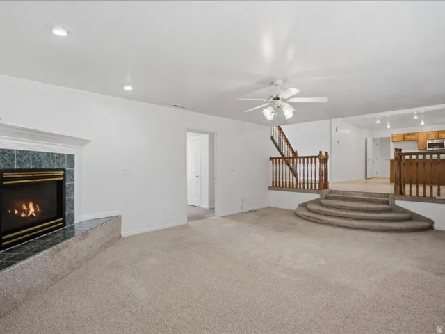 Corner fireplace with tile surround, recessed lighting, ceiling fan, and carpeted flooring