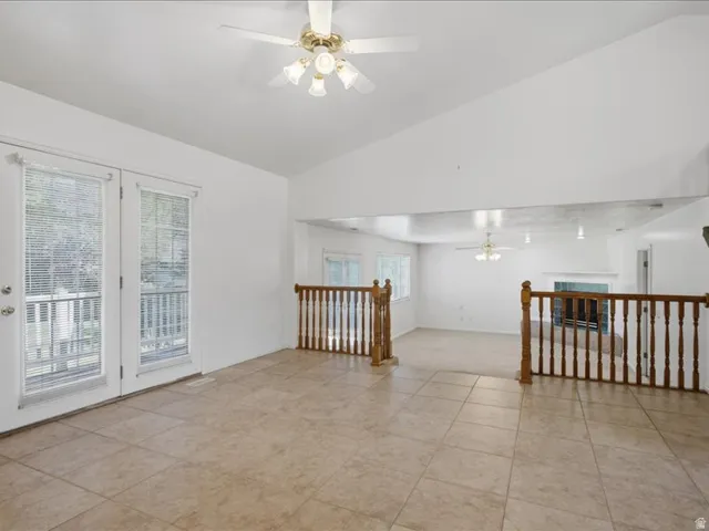 Vaulted ceiling, ceiling fan, tile flooring, white double doors, and wood balusters