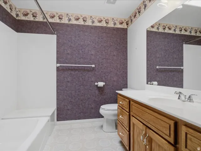 Built-in bathtub with shower, wood-finish vanity with countertop, and integrated sink with chrome fixtures