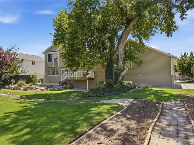 Expansive backyard featuring a manicured lawn, established landscaping, a wood-finish deck, and a concrete patio