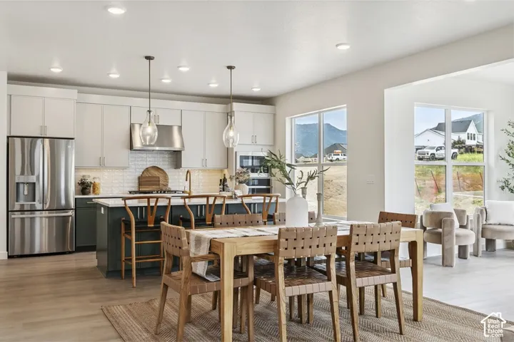 Open-concept kitchen and dining area featuring stainless steel appliances, a large island with seating, pendant lighting, and wood-finish flooring