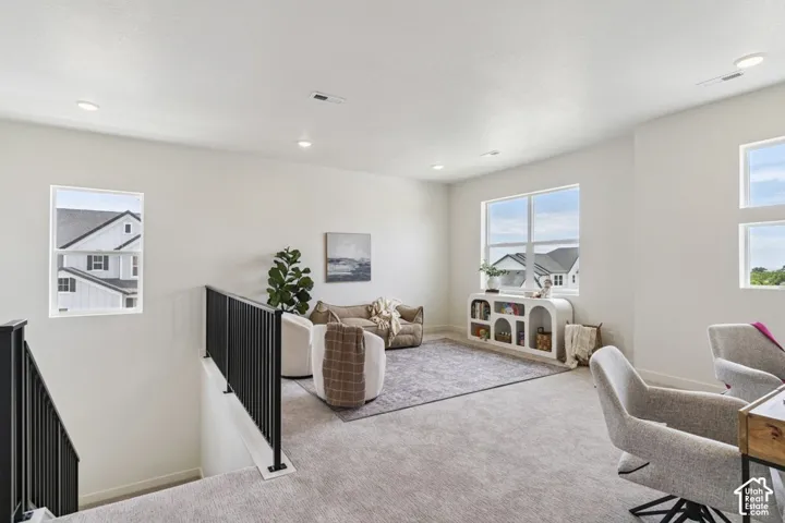 Carpeted loft area with recessed lighting, multiple windows, and black metal stair railing