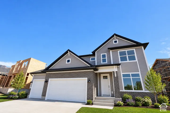 Contemporary exterior with gray siding and dark brick accents, featuring a two-car garage with white doors, a white main entry door, and a concrete driveway