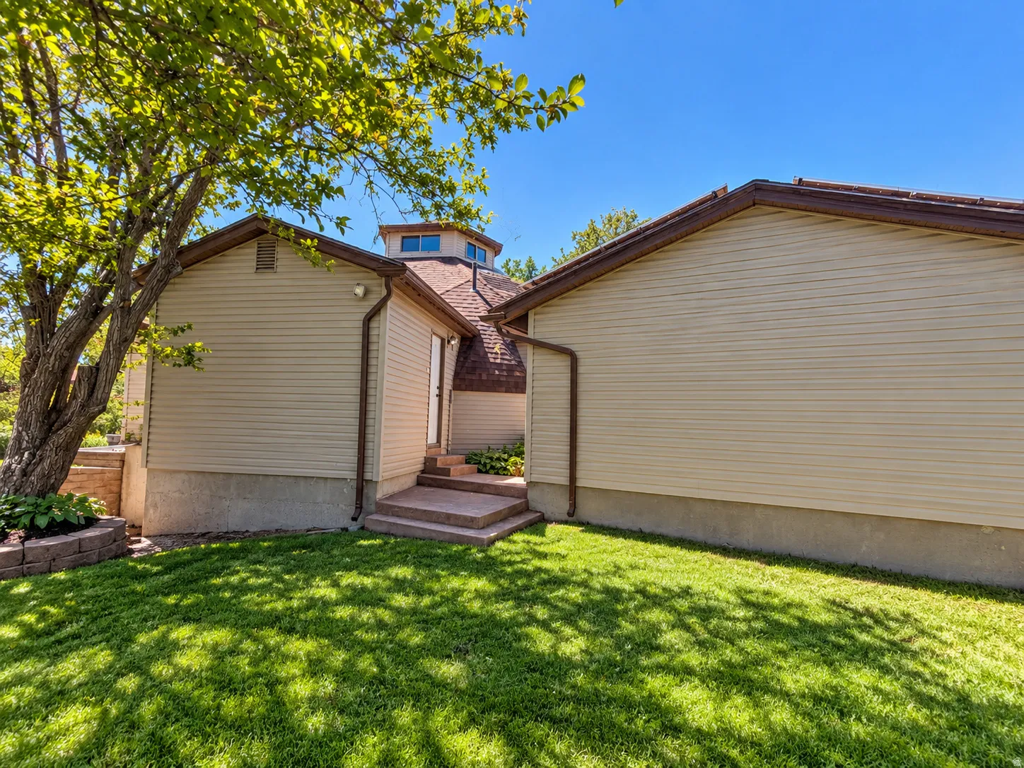 Walkway from house to the detached garage. Manicured lawn, mature tree, concrete steps, concrete foundation, and a unique octagonal roofline with windows