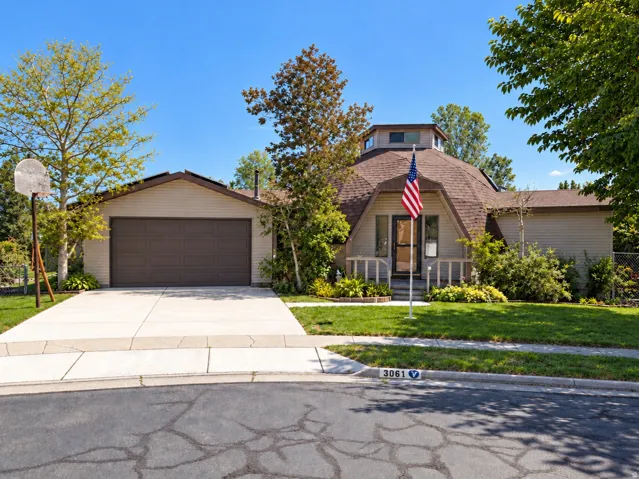 Dome-shaped architectural style, attached garage, concrete driveway, front porch with railing, and mature landscaping