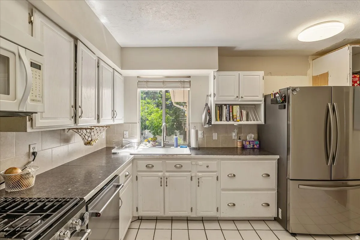 White cabinetry, dark countertops, built-in microwave, stainless steel refrigerator, and tiled flooring