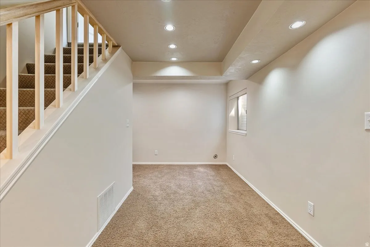 Carpeted flooring extending through the space, light-toned walls, recessed ceiling lighting, and a staircase with a wooden handrail