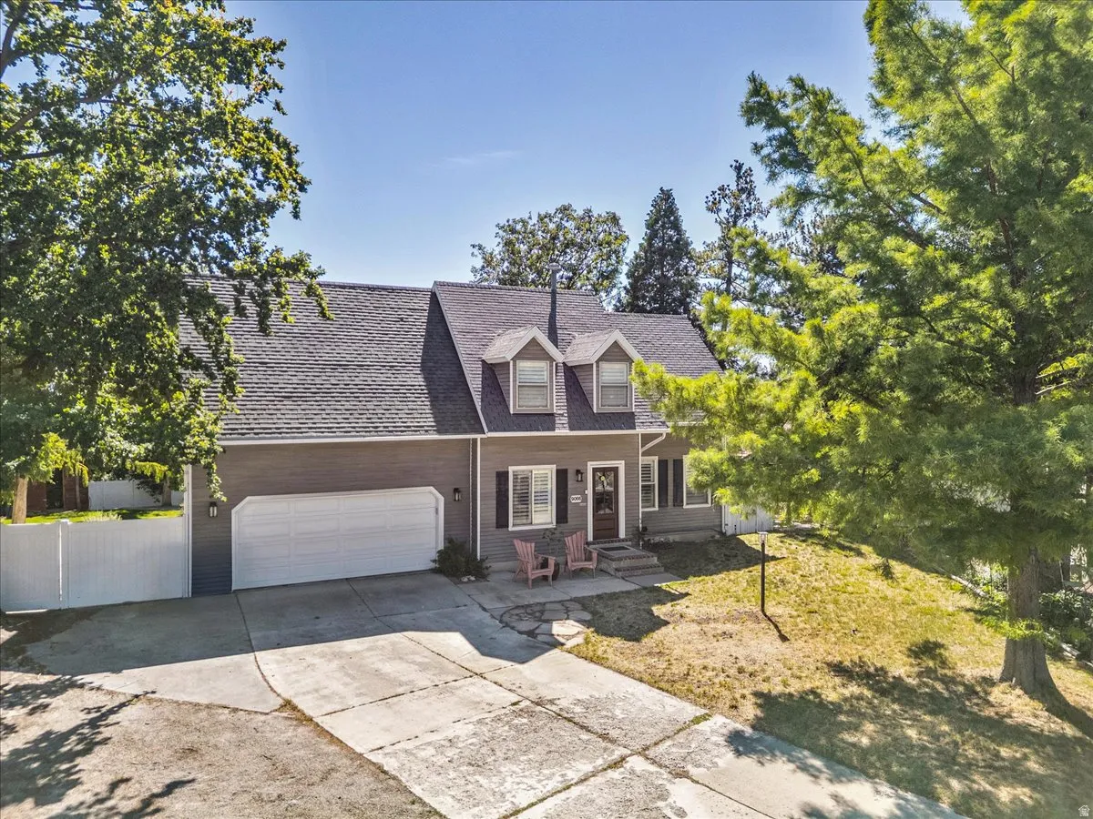 Gabled roofline, dormer windows, attached two-car garage, concrete driveway, and mature landscaping