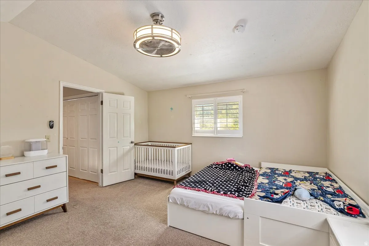 Carpeted bedroom featuring a double bifold closet, a window with plantation shutters, and a ceiling fan with integrated lighting