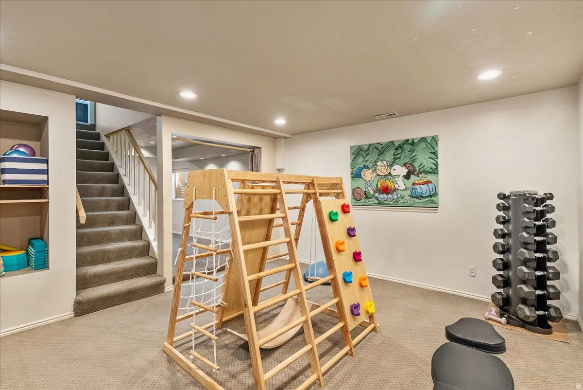Carpeted flooring, recessed lighting, built-in shelving, white baluster staircase, and a doorway opening to an additional room