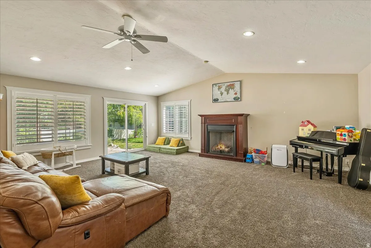 Vaulted ceiling with a ceiling fan and recessed lighting, brown wood-finish fireplace, and sliding glass door leading to a patio